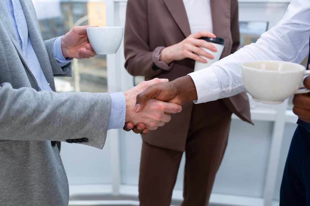 A professional handshake between colleagues holding coffee cups, symbolizing collaboration.